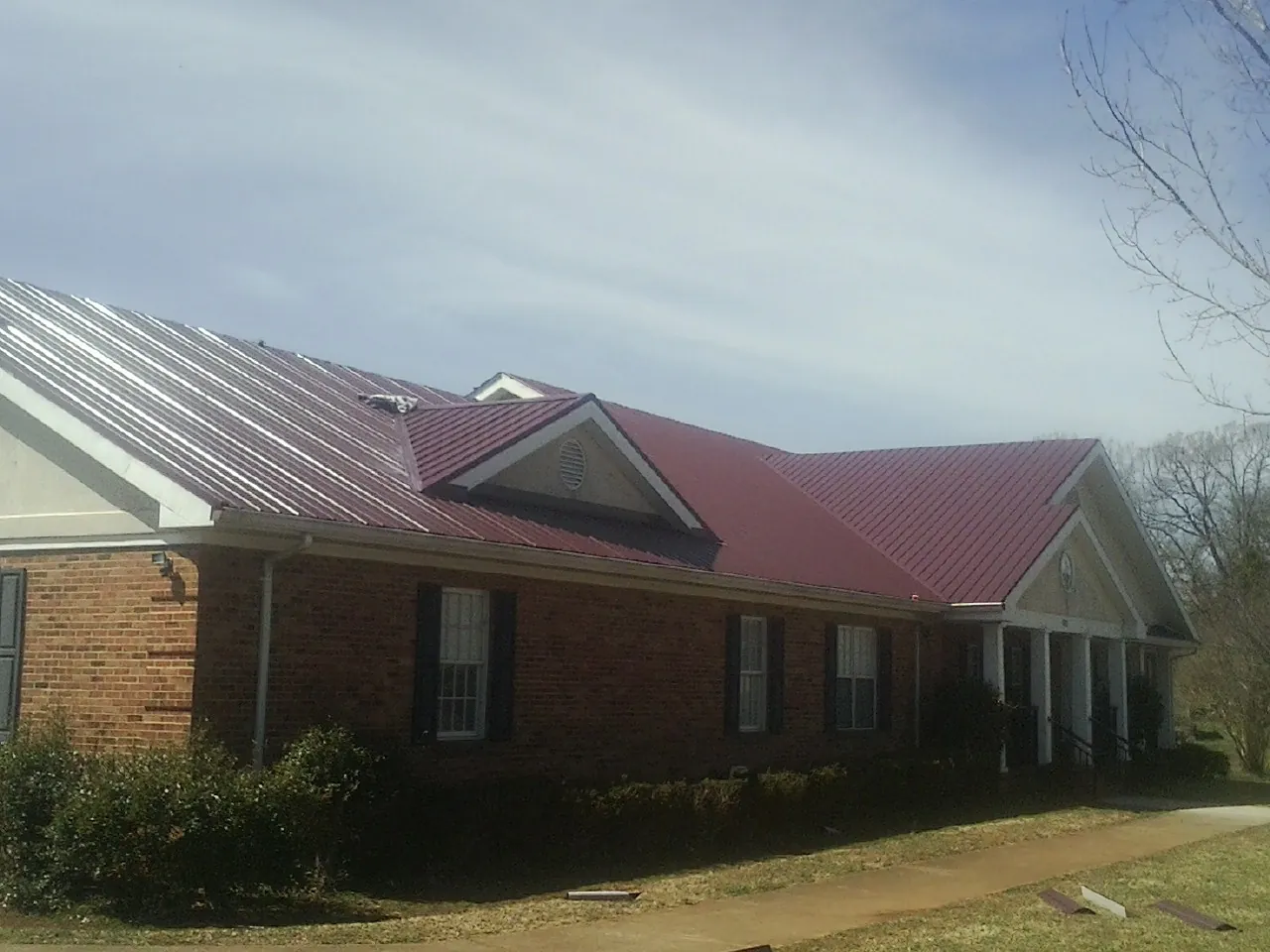 Red metal roof with gabled entries on a long brick building, from a Hail Damage Roof Repair job in Ballico