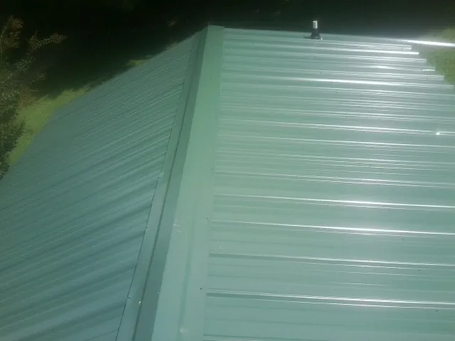 New green metal panels meeting at the ridge of a roof — Flat Roof Repair work by our crew in Ballico