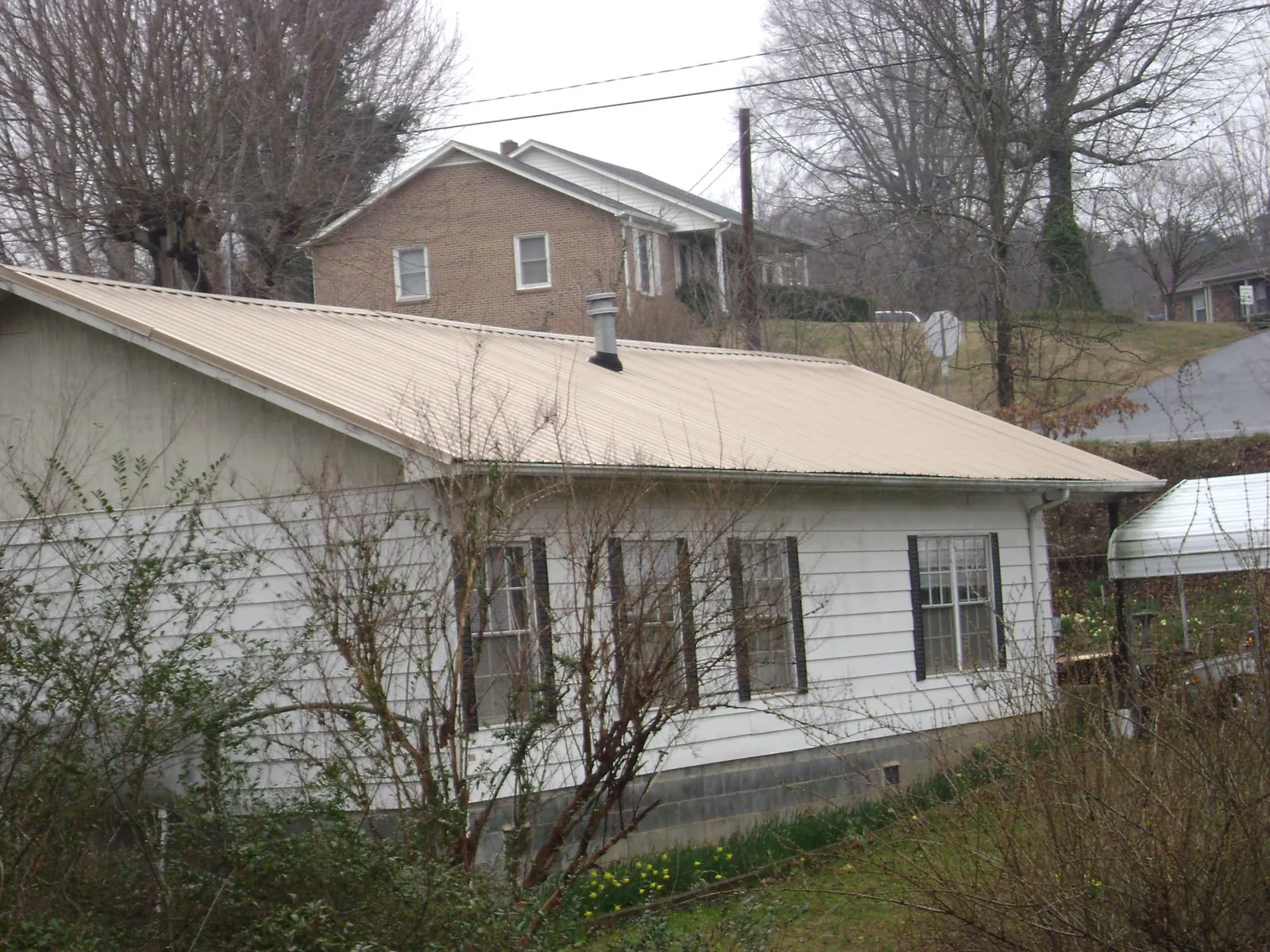 Tan metal roof on a white sided house set into a hillside — Commercial Roofing by Roofing Brothers in Ballico