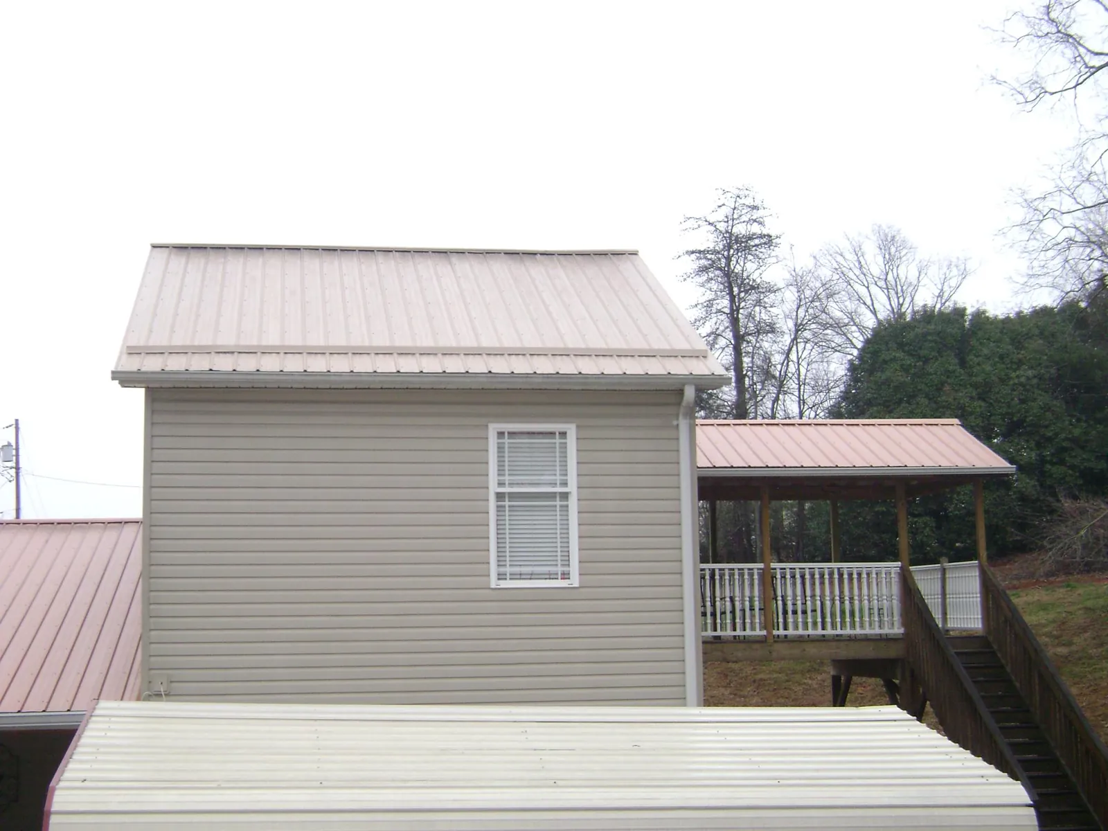 Tan metal roofs on a two story addition and attached porch, from a Roof Replacement job in Ballico
